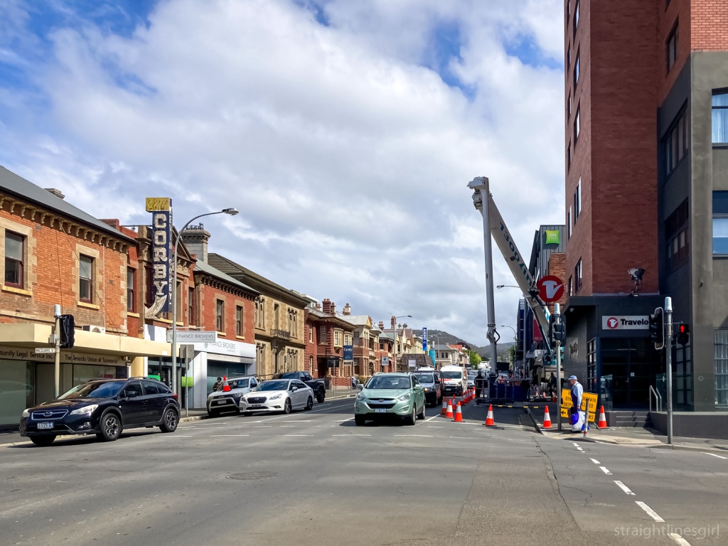A street scene with a large orange brick building on the right and a crane working onsite, and a row of low brick buildings on the left