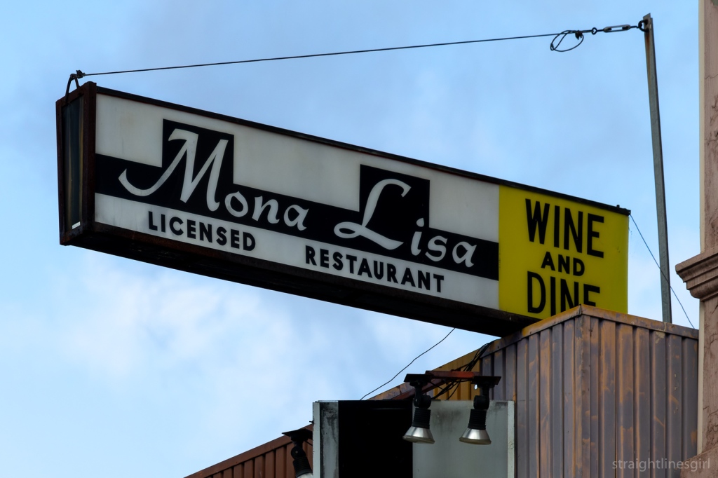 An old neon sign for the Mona Lisa Licensed restaurant, with the words WINE AND DINE in black text on a yellow background