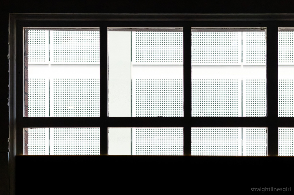 A view through a window to a white metal mesh wall