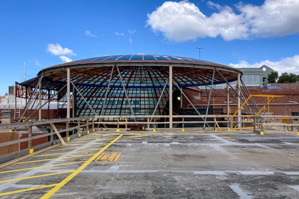 A view across a car park at a partially deconstructed glass and timber dome