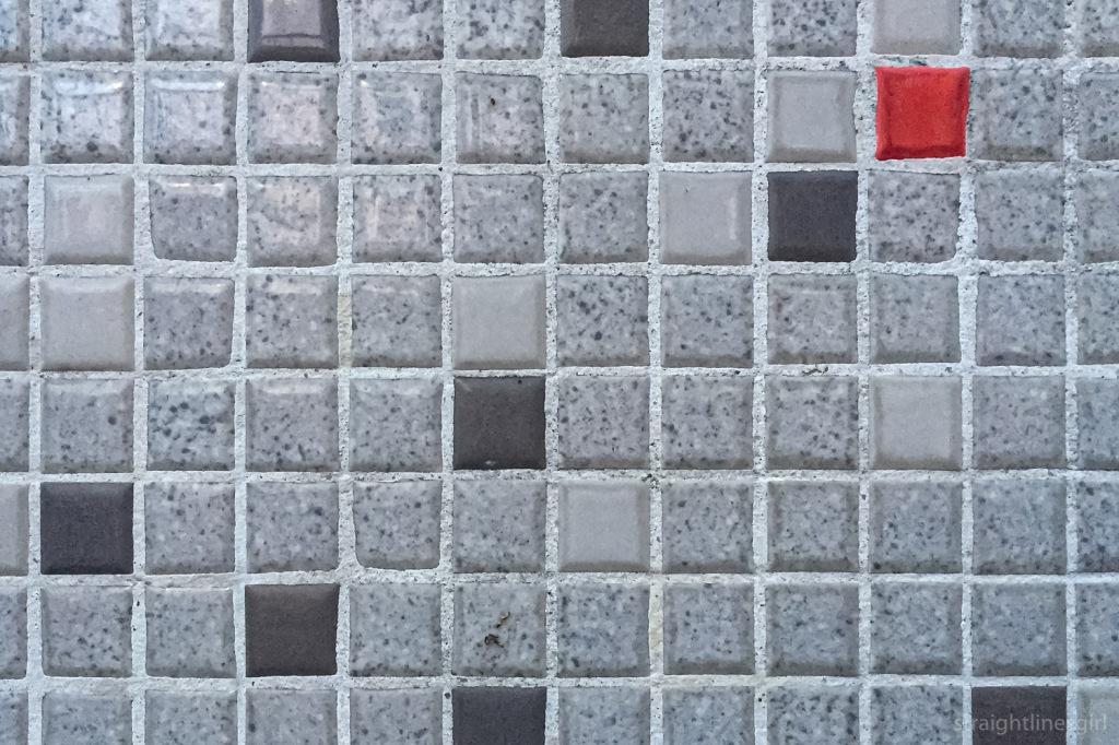 Mural of small grey tiles alternating with lighter grey, darker grey and one red tile