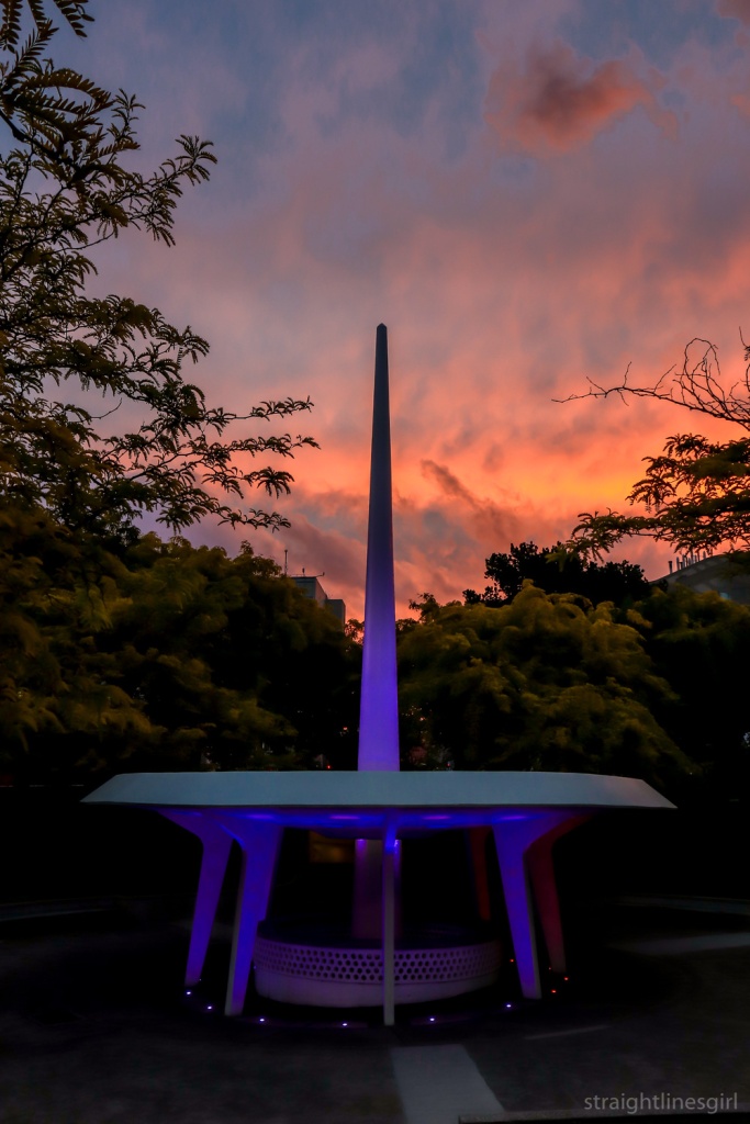 A space needle design fountain lit up at night with the sunset sky in the background)