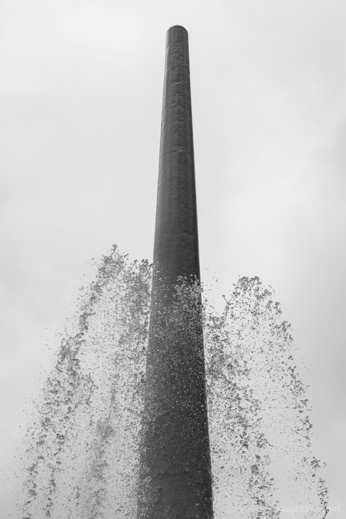 Black and white image of water jets below a tall fountain spire