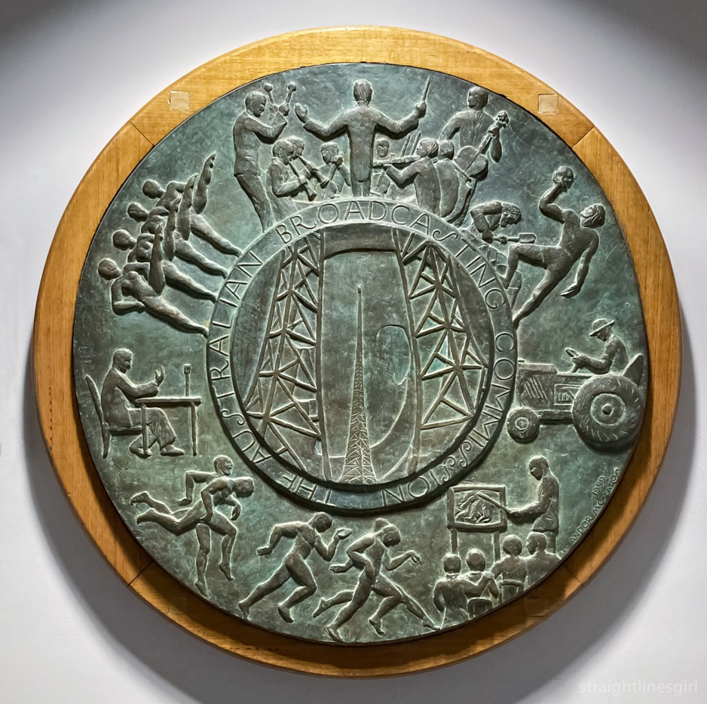 A round plaque depicting the seven stream of ABC activity with a transmission tower in the centre