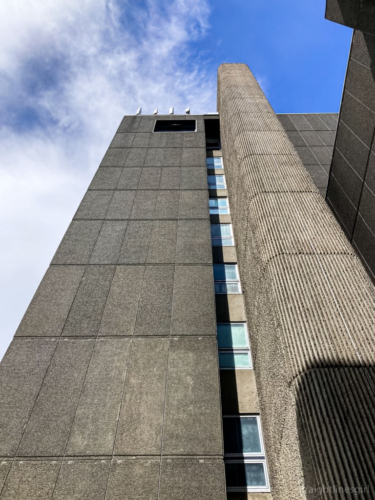 A tall, brutalist building. View is looking up to the sky. 