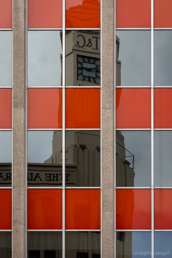 A reflection of an art deco style building in an orange glass curtain wall